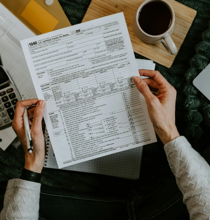 Hands holding tax forms with calculator and laptop.